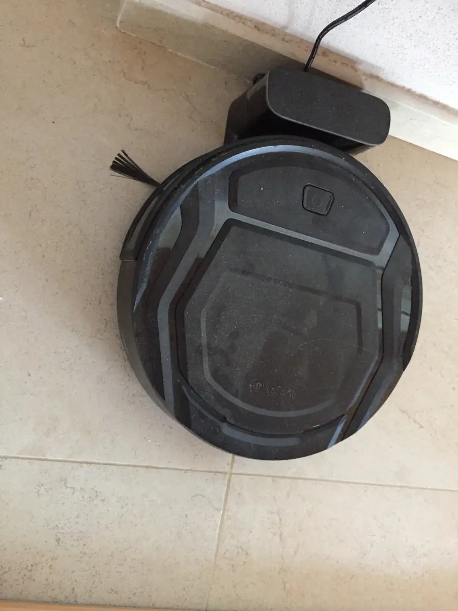 Robot aspirador visto desde arriba trabajando sobre un suelo de baldosa claro